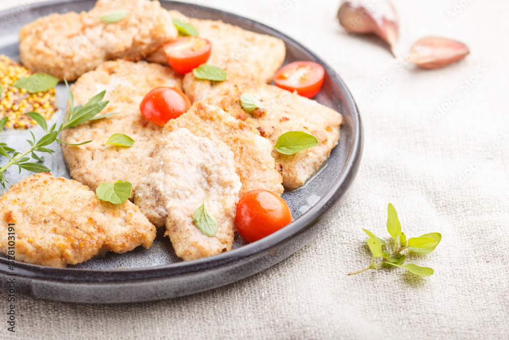 Fried pork chops with tomatoes and herbs on a gray ceramic plate on a black concrete background. side view, selective focus.