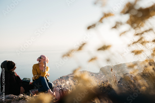 Lifestyle portrait of two best friends, smiling and having fun together. Outdoor photo of two young women, one with hijab, enjoying each other company with old city of Dubrovnik in background.