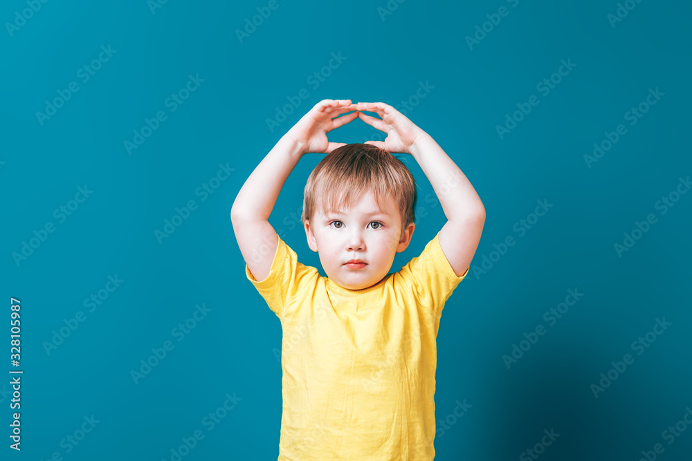 A handsome boy folded his arms over his head in the form of a house on blue background A handsome boy folded his arms over his head in the form of a house on blue background