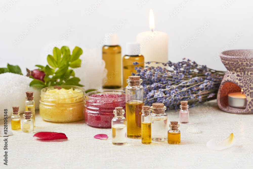 Aromatherapy products. A set of essential oils, scrub jars, lavender, dogrose, a white towel, an aromatherapy lamp, rose petals, a burning candle stand on a light table Aromatherapy products. A set of essential oils, scrub jars, lavender, dogrose, a white towel, an aromatherapy lamp, rose petals, a burning candle stand on a light table