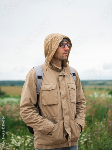 Man with hands in pockets standing in field looking away