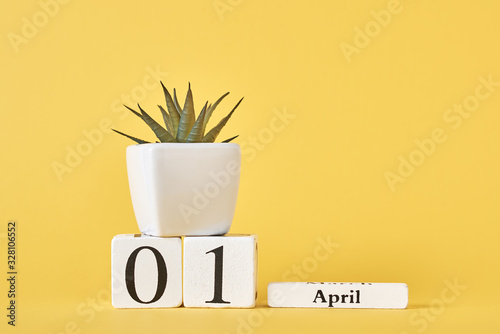Wooden blocks calendar with date 1st april and plant on the yellow background. April fools day concept