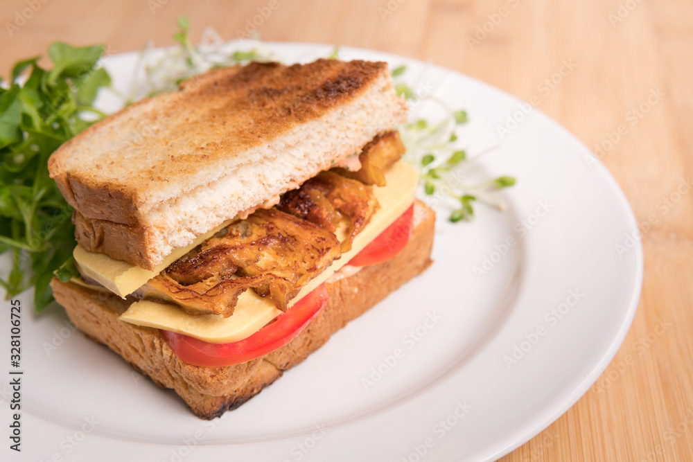 Vegan sandwich for breakfast, healthy & delicious food for plant based, vegan and vegetarian diet. Ingredients are toasted bread, vegan cheese, fried tofu, tomato, iceberg lettuce and kaiware sprouts.