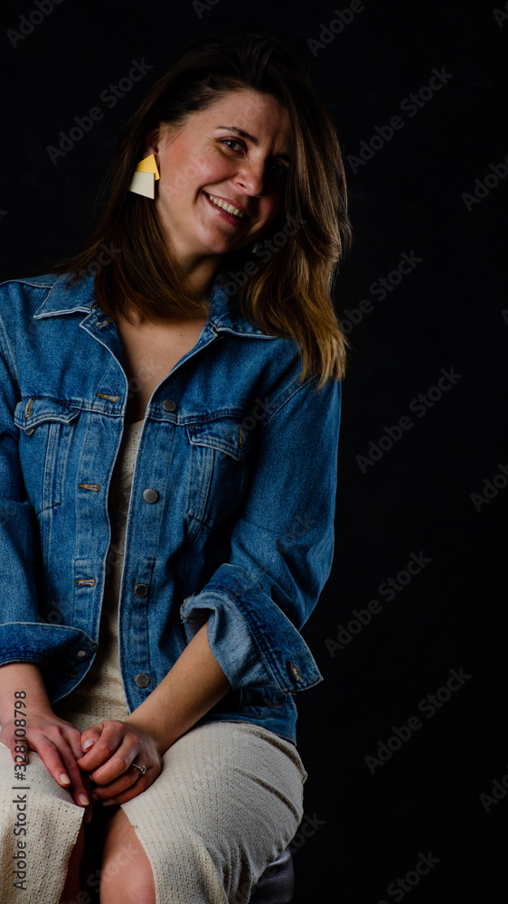 Young beautiful woman wearing in a black leather jacket, black top, short skirt and boots posing over black background. Studio shot of blonde woman against black background Young beautiful woman wearing in a black leather jacket, black top, short skirt and boots posing over black background. Studio shot of blonde woman against black background
