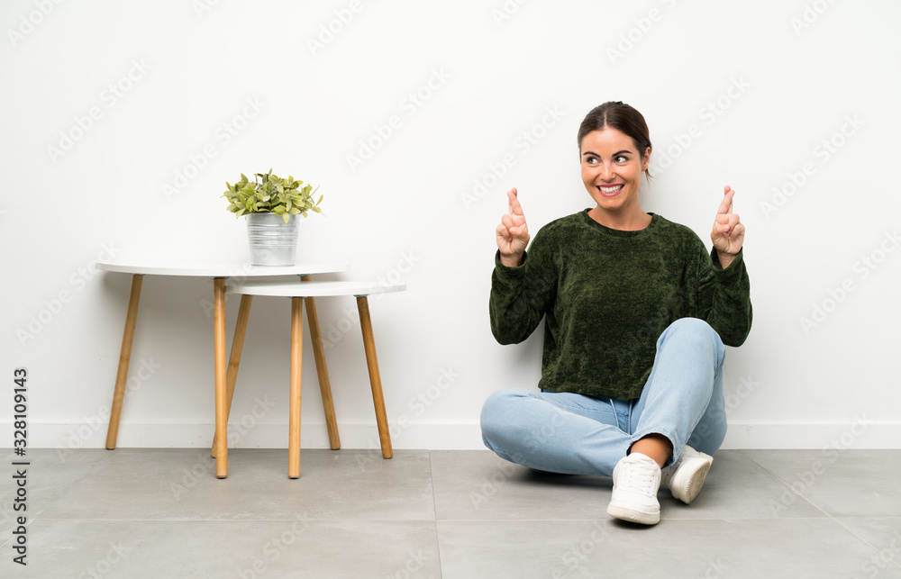 Young woman sitting on the floor with fingers crossing Young woman sitting on the floor with fingers crossing