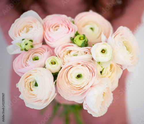 A girl in a pink dress is holding a bouquet of delicate Ranunculus flowers.