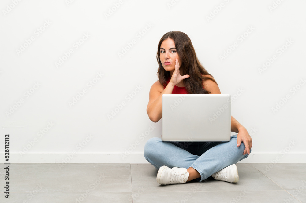 Young woman with a laptop sitting on the floor whispering something Young woman with a laptop sitting on the floor whispering something