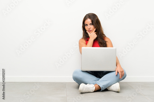Young woman with a laptop sitting on the floor thinking an idea © luismolinero