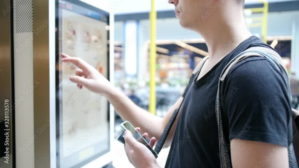 Young man makes an order using a digital screen. Modern food ordering technology through a special service without operators Young man makes an order using a digital screen. Modern food ordering technology through a special service without operators