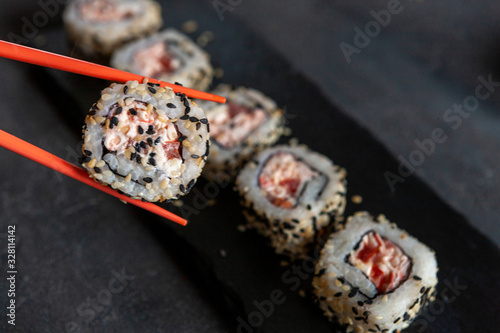 Japanese crab meat mousse sushi on stone board with chopsticks. Top view, close up on black concrete background.