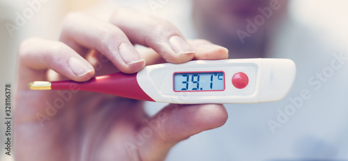 Flu and corona concept: Man is holding a fever thermometer in his hand, close up