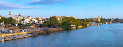 Panoramic view of the waterfront of the Guadalquivir River in Seville, Andalusia, Spain. On a warm winter evening, people relax and stroll along the waterfront.