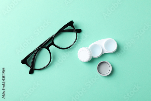 Glasses and contact lenses on mint background, top view