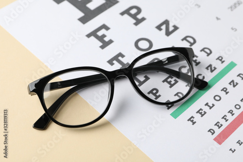 Glasses and eye test chart on beige background, close up