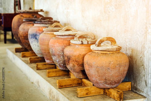Row of earthen jars with wood lids and rough gray floor for water storage in Asian house. Selective focus on wood lids.