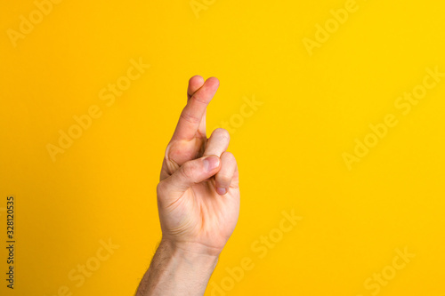 hoping for the best. close up hand with fingers crossed against yellow background with copy space