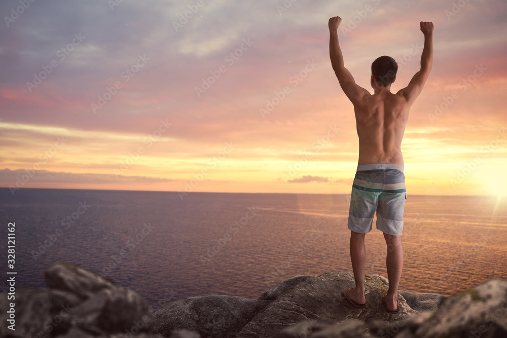 Man with raised arms standing on a cliff over the sea