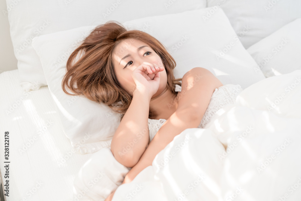 Naklejka premium Portrait of beautiful Asian woman with attractive smile enjoy fresh soft bedding linen mattress in white bed room modern apartment. Cute asia girl sleep resting, good night sleep concept.