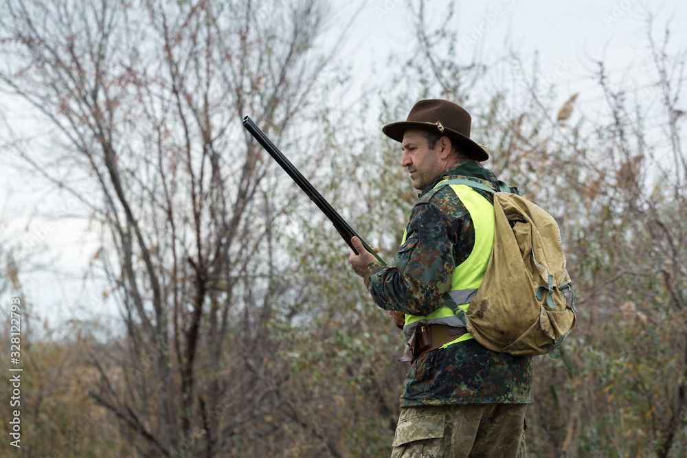 Hunting period, autumn season open. A hunter with a gun in his hands in hunting clothes in the autumn forest in search of a trophy. A man stands with weapons and hunting dogs tracking down the game. Hunting period, autumn season open. A hunter with a gun in his hands in hunting clothes in the autumn forest in search of a trophy. A man stands with weapons and hunting dogs tracking down the game.