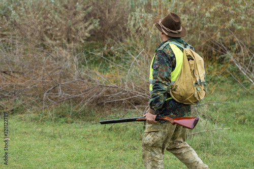 Hunting period, autumn season open. A hunter with a gun in his hands in hunting clothes in the autumn forest in search of a trophy. A man stands with weapons and hunting dogs tracking down the game.