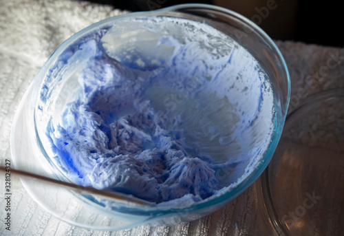  Hair dye product. Bleach for hair. Bowl with peroxide and brush, closeup on a purple background. 