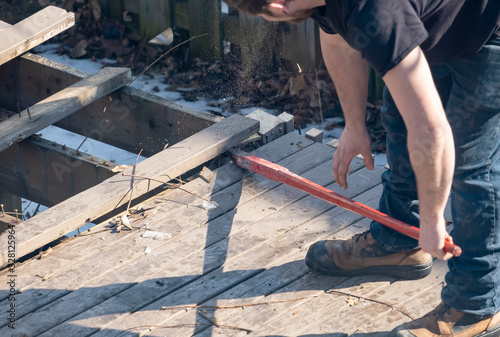Obraz na plátně Man Dismantling an Old Wooden Deck with a Red Crowbar in a Backyard