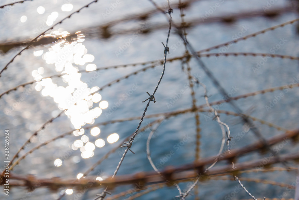 Rusty nato wire, rusty barbed wire, water in the background, border, abstract Rusty nato wire, rusty barbed wire, water in the background, border, abstract