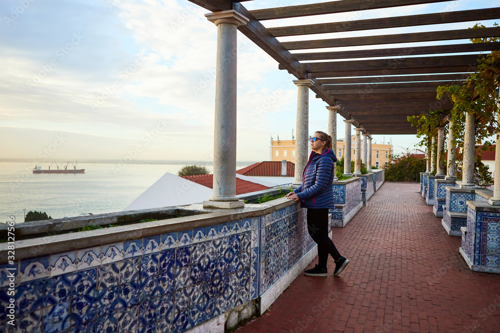 Fototapeta premium Beautiful women tourist looks at the red roofs of Lisbon from the viewpoint Miradouro de Santa Luzia