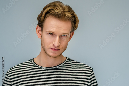 Close up studio portrait of young handsome confident blond man wearing striped  t-shirt, posing against light gray background. Copy, empty space for text