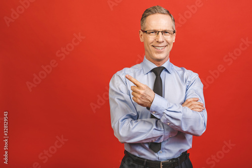 Follow me! Look here! Close up portrait of cheerful satisfied pleased qualified experienced joyful aged businessman pointing on empty blank place isolated on red background.