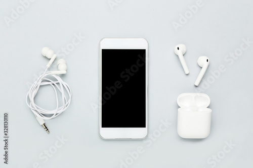 White wireless earbuds with earphones and mobile phone on grey background photo