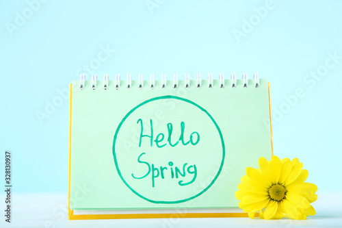 Chrysanthemum flower and notepad with text Hello Spring on blue background