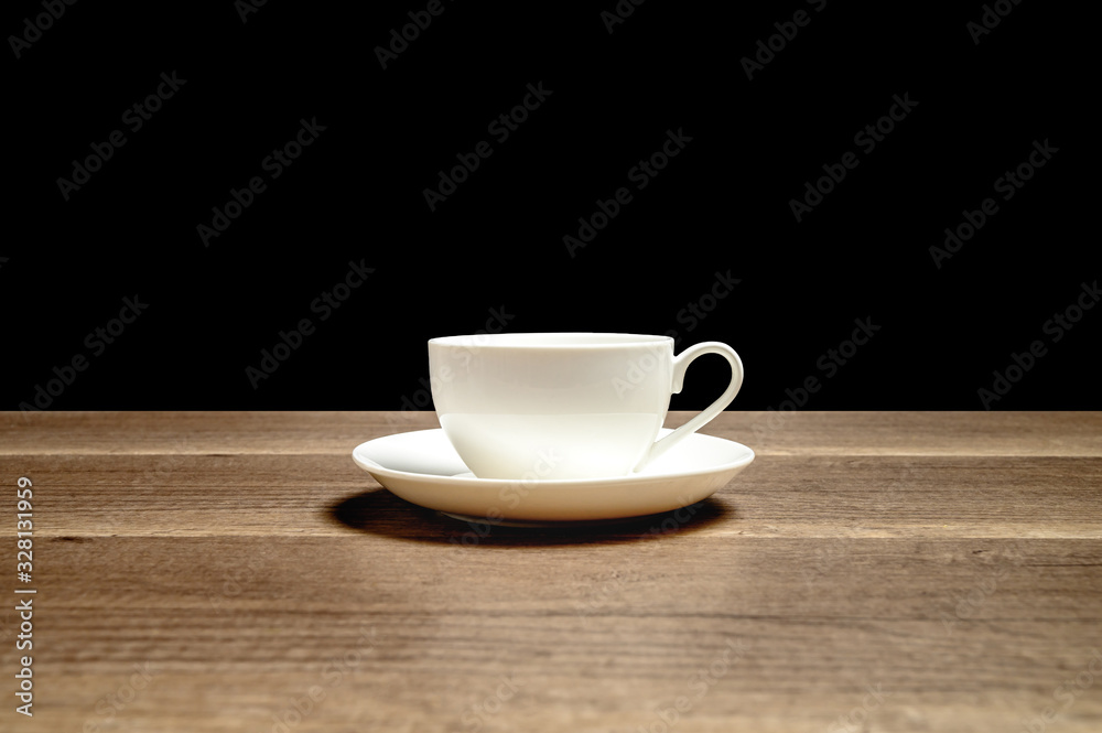 White glossy ceramic cup on saucer placed on wooden table with black background White glossy ceramic cup on saucer placed on wooden table with black background