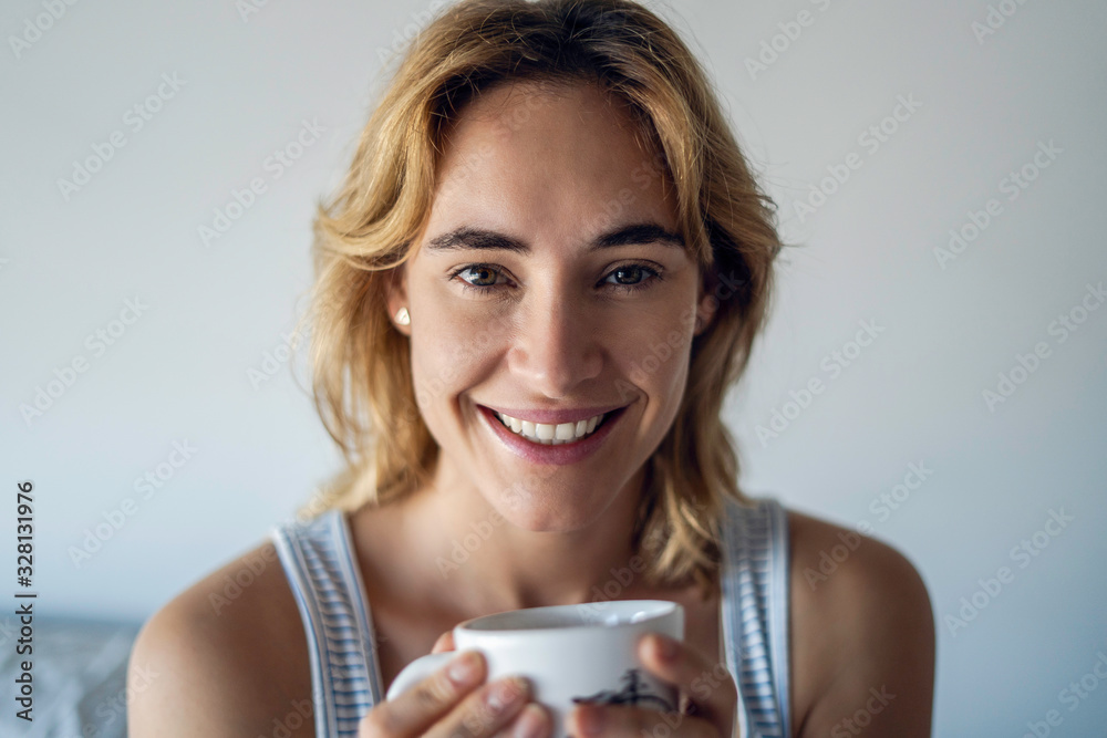 Portrait of smiling young woman holding coffee mug in bedroom Portrait of smiling young woman holding coffee mug in bedroom