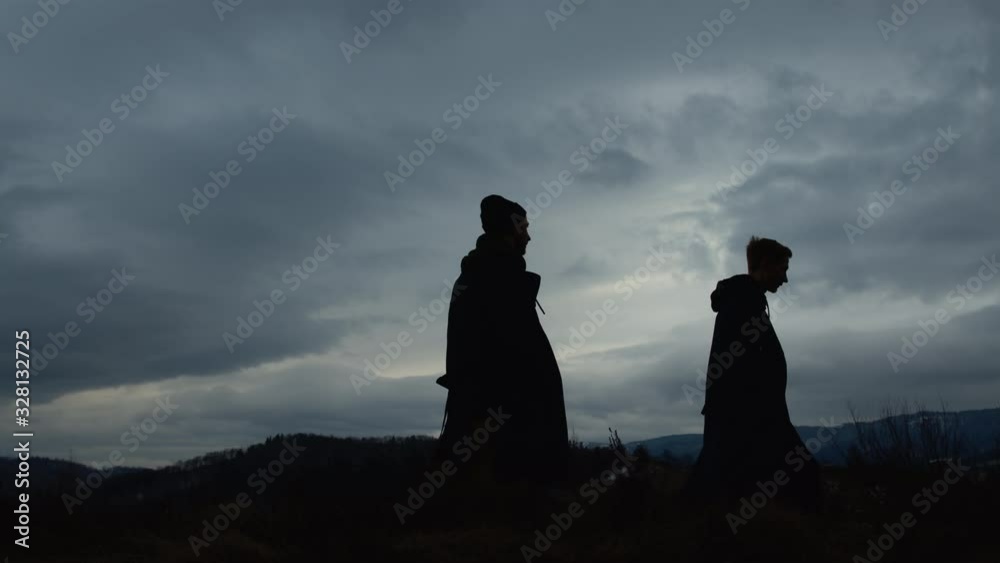 Two Friends Are Walking In Nature On Background Of Cloudy Sky At Dusk.