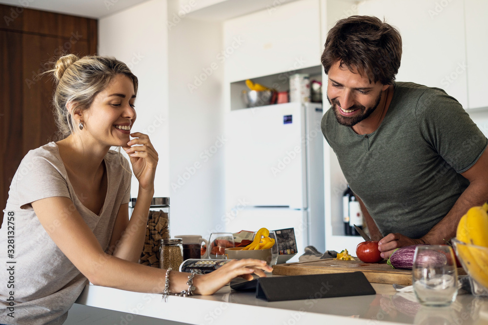 Happy young couple using digital tablet while cooking in kitchen Happy young couple using digital tablet while cooking in kitchen