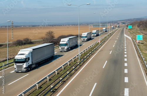 Convoy of many White transportation trucks in line as a caravan or convoy on a countryside highway under a blue sky