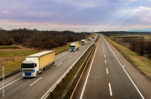 Convoy or caravan of transportation trucks on a highway on a bright blue day. Highway transportation with lorry tracks