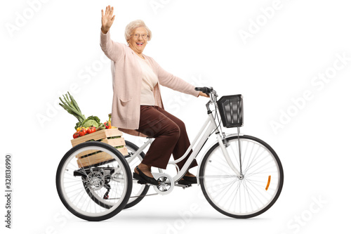 Elderly lady riding a tricycle with a crate full of fruits and vegetables and waving at the camera