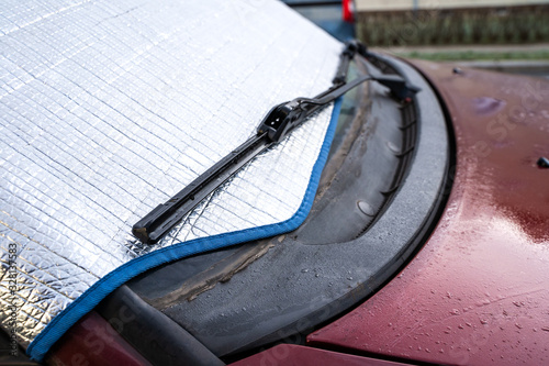 Protected windshield and wipers of a red car on winter morning
