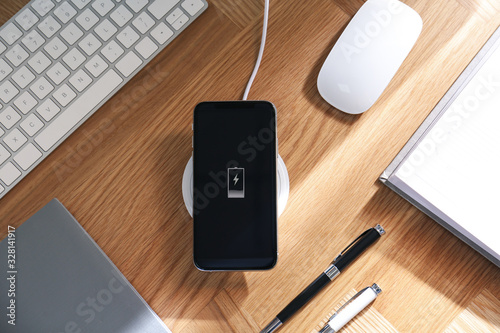 Photography Smartphone charging with wireless pad, flat lay. Modern workplace