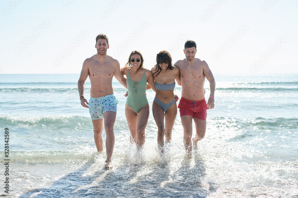 Four happy friends walking together and splashing water on beach Four happy friends walking together and splashing water on beach