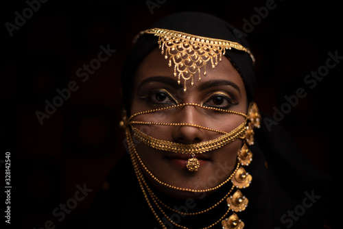 Conceptual middle eastern face portrait of a woman adorned with golden jewelry in black studio background.  conceptual model photography.