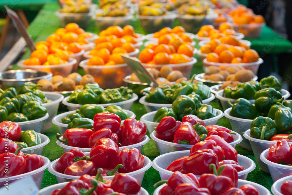 Red and green peppers and fruits for sale in bowls on a market stall.