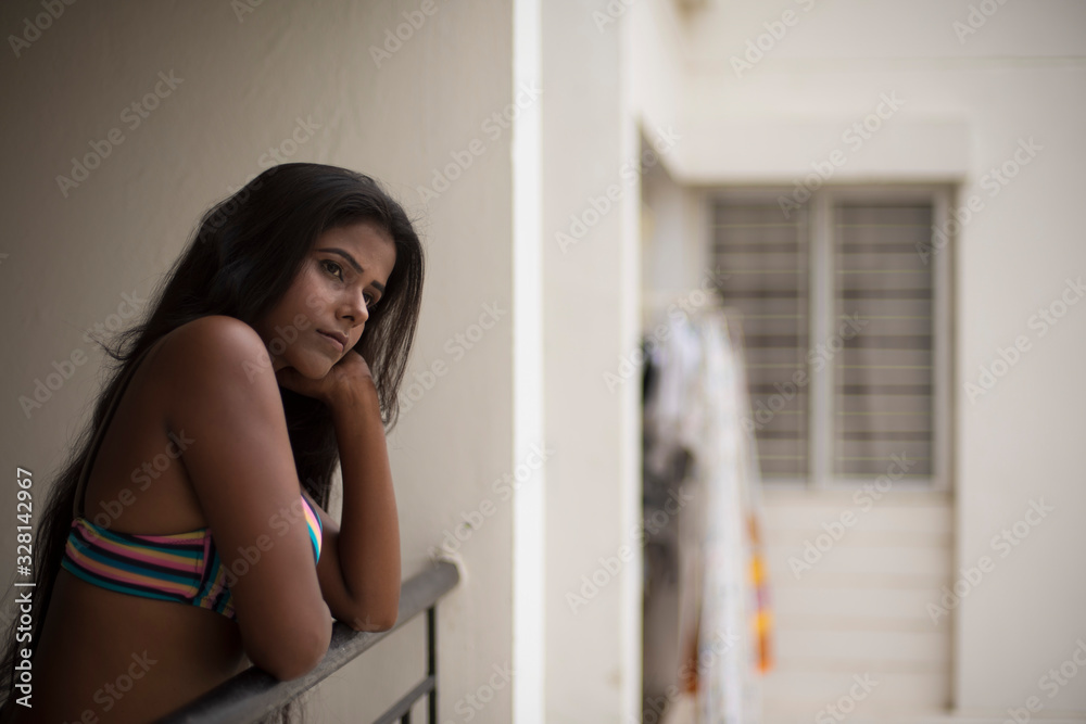 Portrait of an young and beautiful dark skinned Indian Bengali woman in colorful lingerie/bikini and hot pants posing in casual mood on a balcony in white urban background. Boudoir photography. Portrait of an young and beautiful dark skinned Indian Bengali woman in colorful lingerie/bikini and hot pants posing in casual mood on a balcony in white urban background. Boudoir photography.