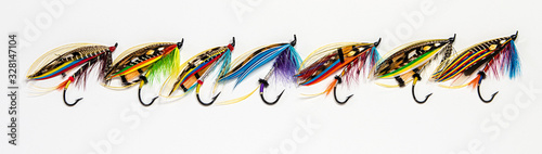 Seven beautiful and colourful fly fishing lures in a lineup on white