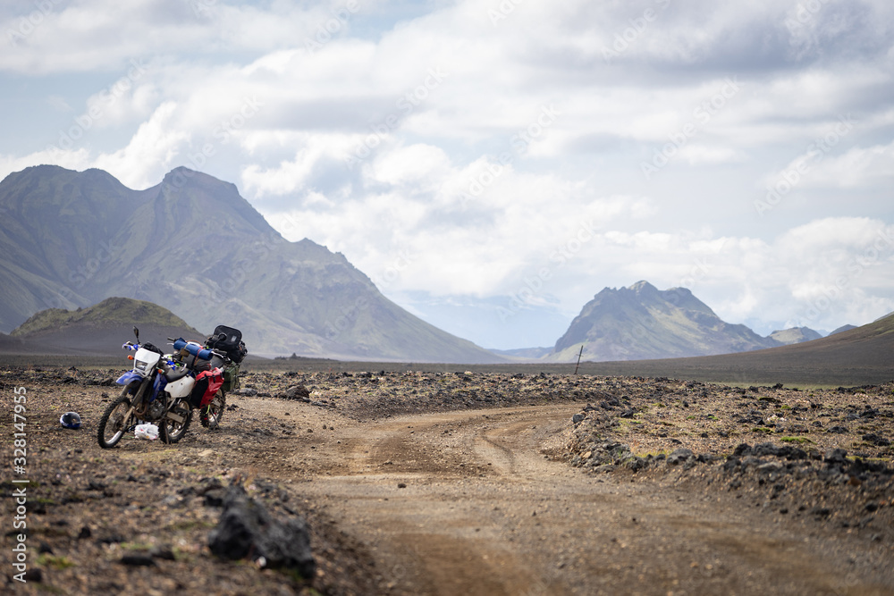 Two enduro Motorcycle standing on a dirt road in the desert surrounded by mountains on the Laugavegur trail, Iceland. off road travel concept, enduro rider equipment, extreme lifestyle