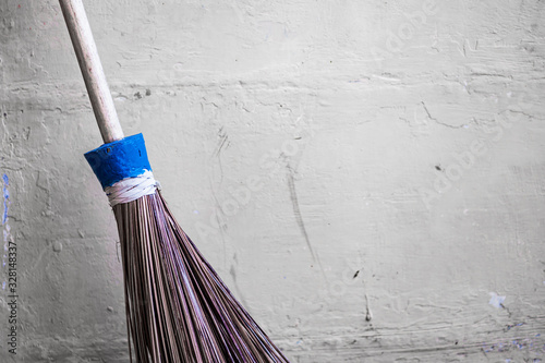 Traditional stick brooms are leaning against a pale yellow concrete wall. Vintage theme background concept.