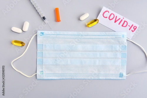 Protection sterile mask and inscription covid-19 thermometer, syringe on gray background. Coronavirus disease named COVID-19. Healthcare concept. Virus vaccine