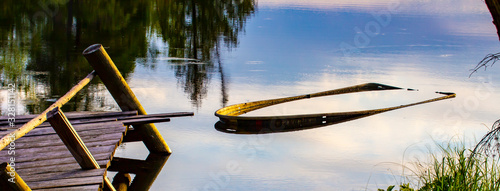 Old rowboat filled with lake water near an old dock with sky reflections photo